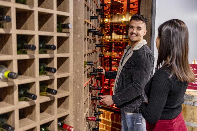 two adults press a wine bottle to reveal a secret door to a wine bar