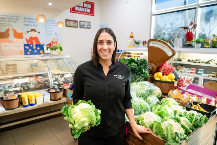 a woman smiling and holding a lettuce next to fresh produce