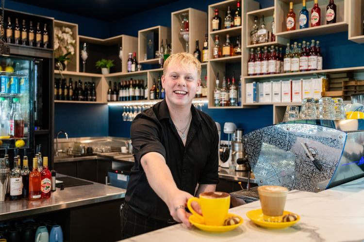 A barista smiling and handing over a cup of coffee