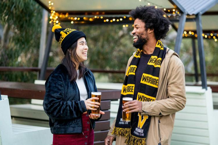 Two adults in Werribee Football Club scarf and beanie with beer