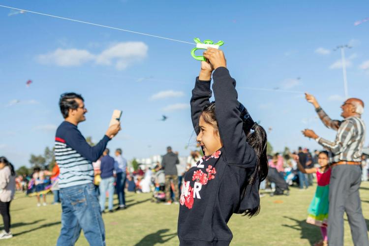 child holding a kite string above their head as their family take photos behind them