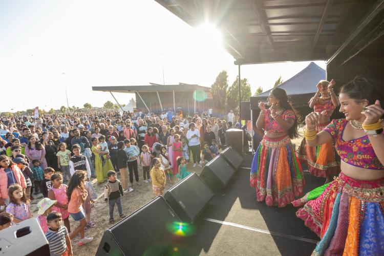 colourful Bollywood dancers performing on a stage in front of a crowd of people outdoors