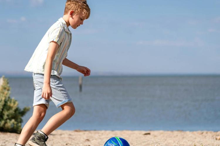 child kicking soccer ball on beach with water in the background at  at Werribee South Foreshore