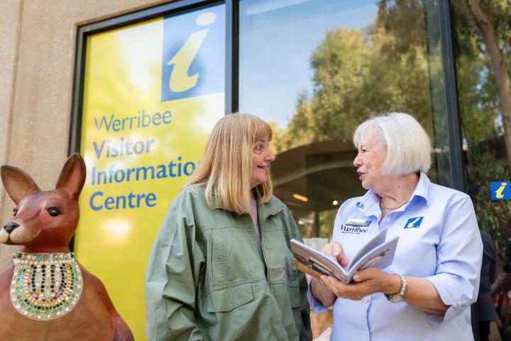 two adults standing outside chatting and holding brochure at the Werribee Visitor Information Centre